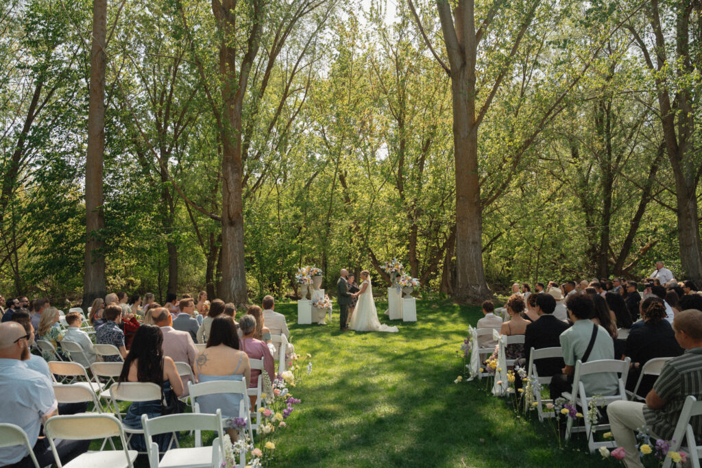 Outdoor wedding ceremony under tall trees at The Cottage at River Bend in Eagle, Idaho.
