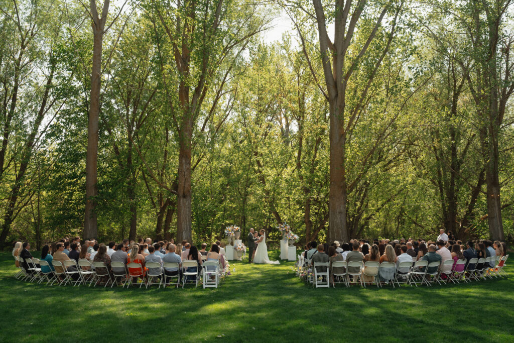 Outdoor wedding ceremony under tall trees at The Cottage at River Bend in Eagle, Idaho.