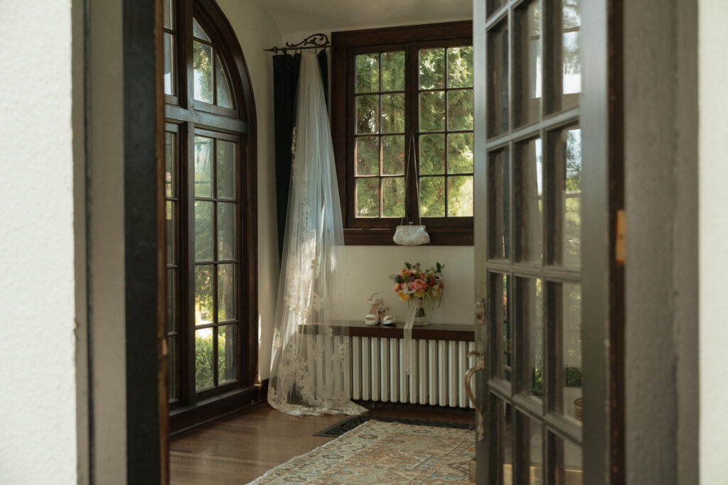 Lace wedding dress hanging by arched windows at The Cottage at River Bend in Eagle, Idaho.
